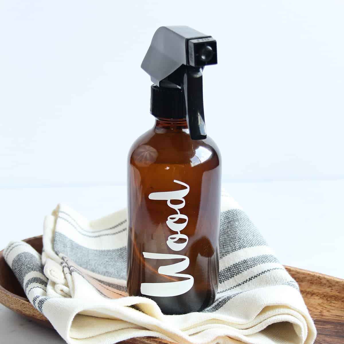 Amber glass spray bottle on a cleaning towel with the word wood in vinyl on the bottle