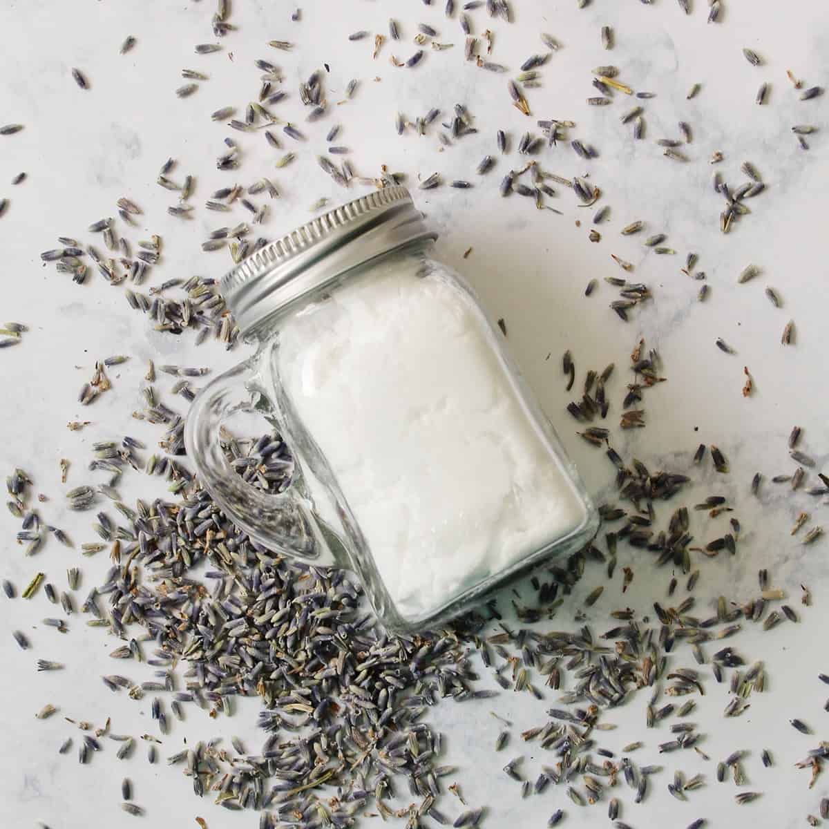 closeup looking down a clear glass jar filled with homemade carpet powder on a counter covered in purple lavender buds