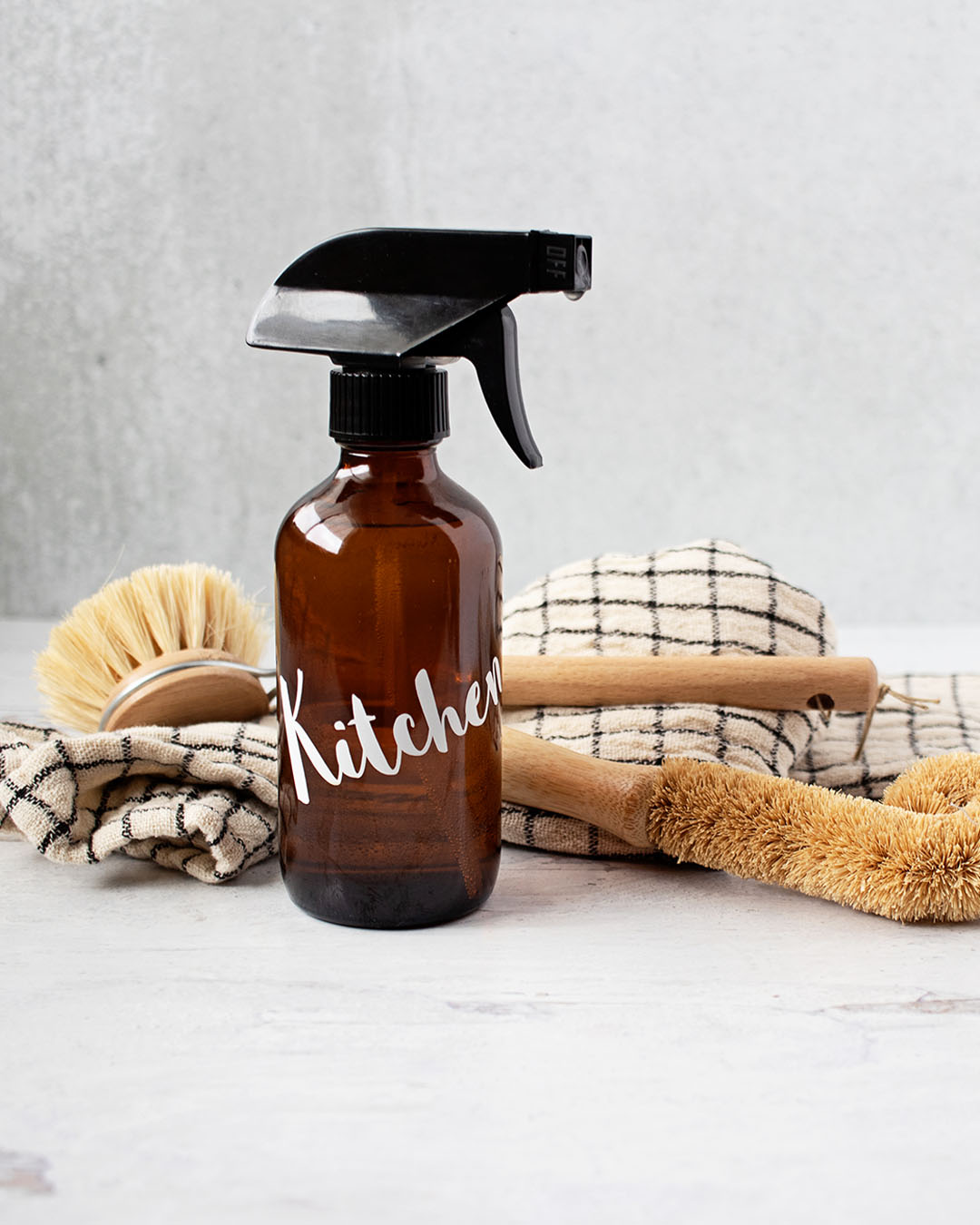 amber glass bottle labeled kitchen in front of natural cleaning brushes and a cloth on a countertop.