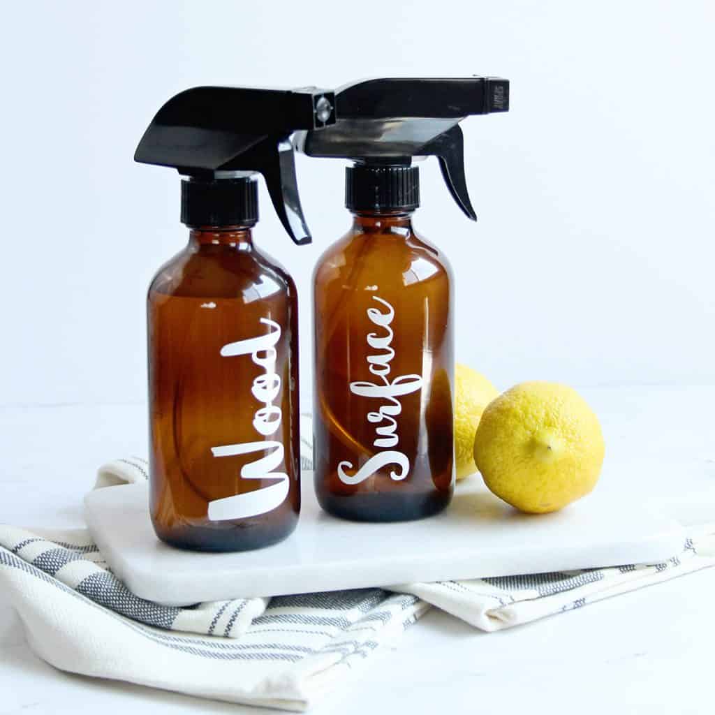 Tall amber glass bottles of handmade cleaning solutions for wood and surfaces next to fresh lemons.