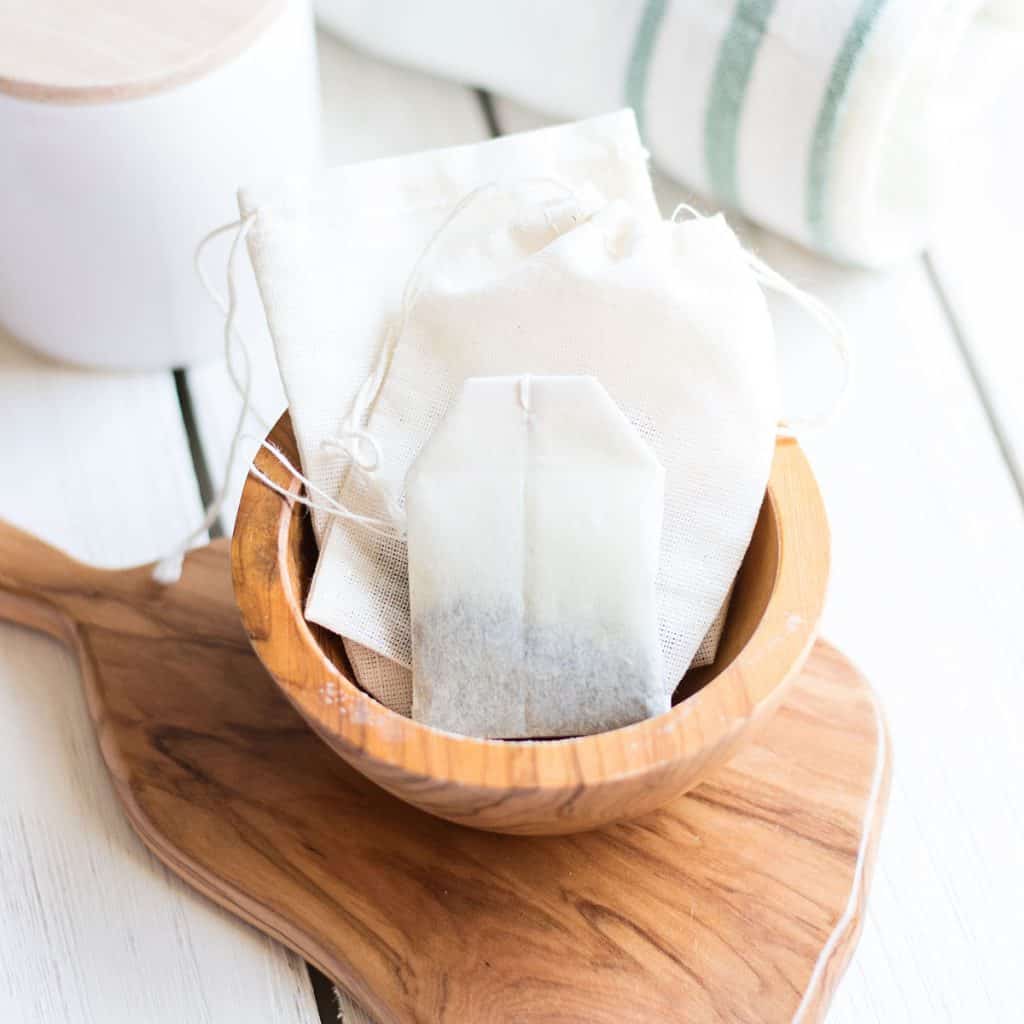 wooden bowl on a cutting board filled with green tea bags in a sunny kitchen nook.