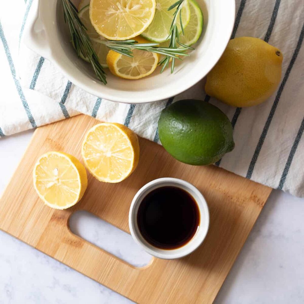 Making fresh citrus Stove Top Potpourri with slices lemons, limes, and sprigs of rosemary, in a bowl on top of linen towel and cutting board.