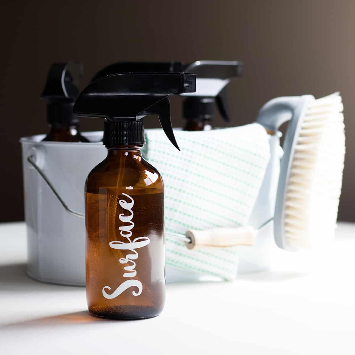 amber glass bottle filled with natural cleaning spray next to a cleaning organizer and brush