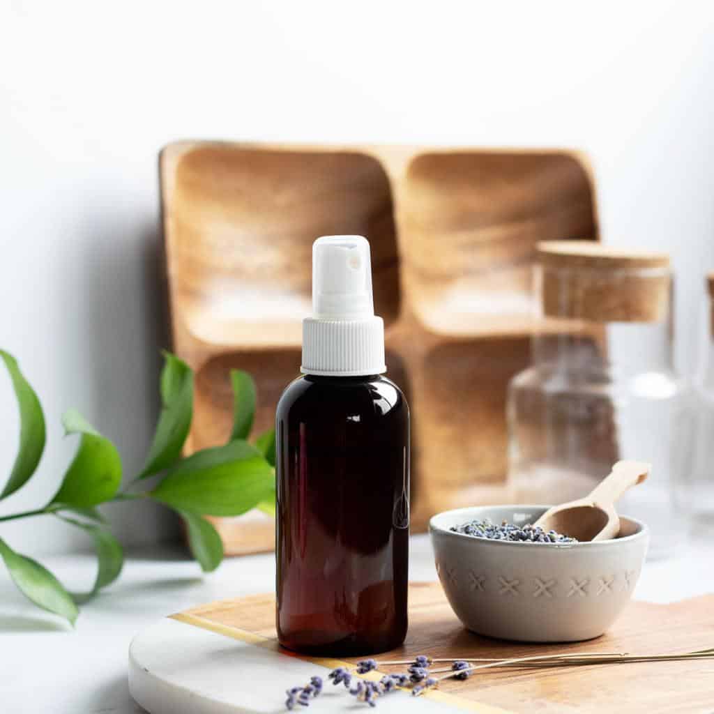 amber glass mist bottle next to bowl of lavender buds and sprigs of lavender in my home studio.