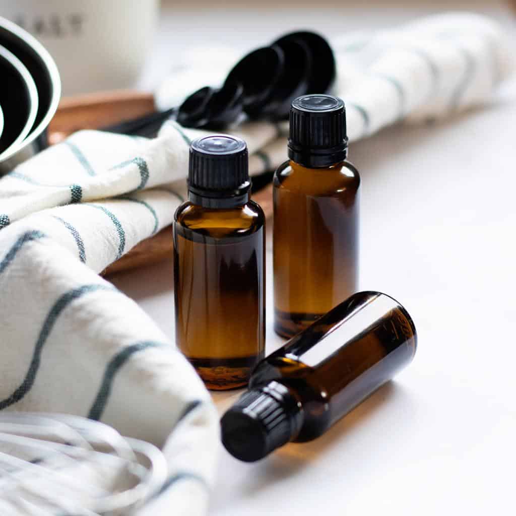 Amber glass bottles with black lids of essential oils next to a cotton towel in front of black measuring spoons.