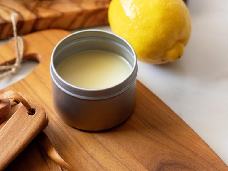 A metal tin of yellow lemon conditioning spoon butter on a wooden cutting board next to a lemon