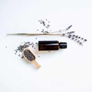 Amber glass bottle of candle fragrance on bright white background next a sprig and scoop of lavender.