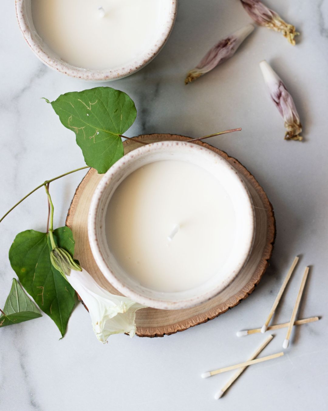 scented candles in white ceramic bowls surrounds by honeysuckle flower stems and match sticks on a marble counter top