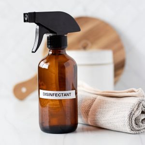 Amber glass bottle labeled disinfectant next to rolled towel on light background