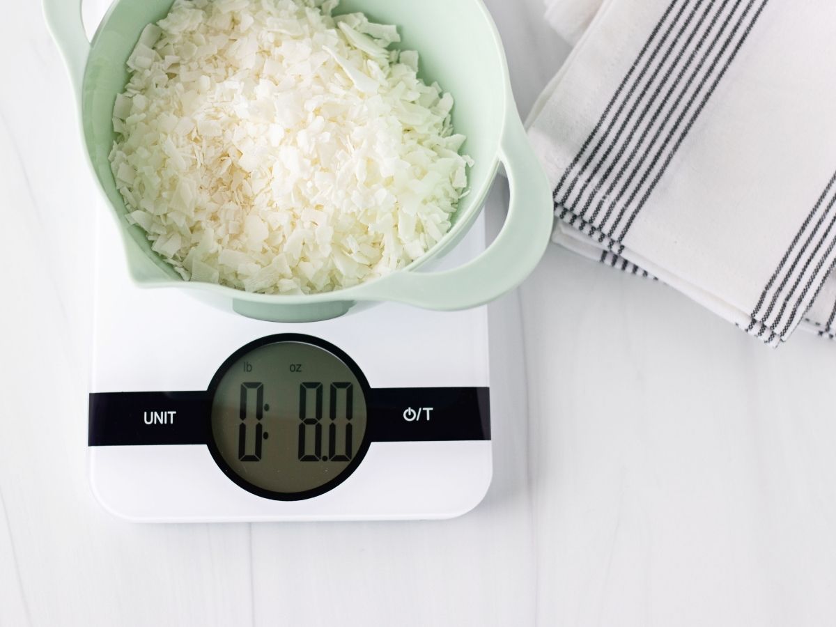 Bowl of soy candle wax flakes on a digital scale next to striped towel