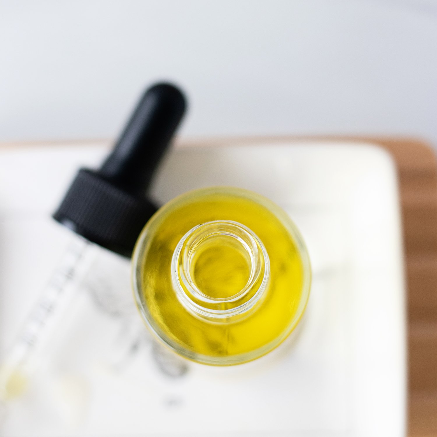 A small glass dropper bottle filled with golden natural hair serum resting on a clean towel.