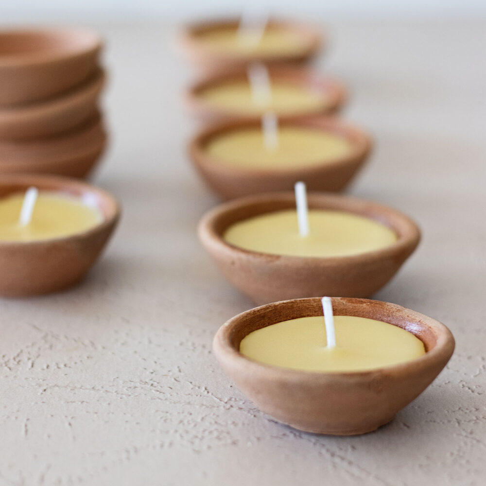 Rows of handmade terracotta candles with a stack of terracotta bowls.