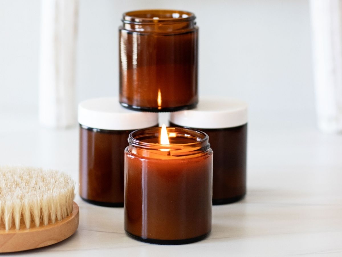four stacked amber glass jar massage candles on a white background with one wick light in front