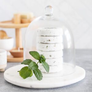 round disk shower steamers with dried green herbs stacked under a glass dome on a round marble board