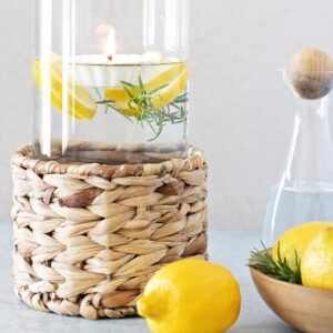 Glass vase filled with yellow lemon slices, green rosemary sprigs, and a floating candle in water that is creating a pretty candle light.