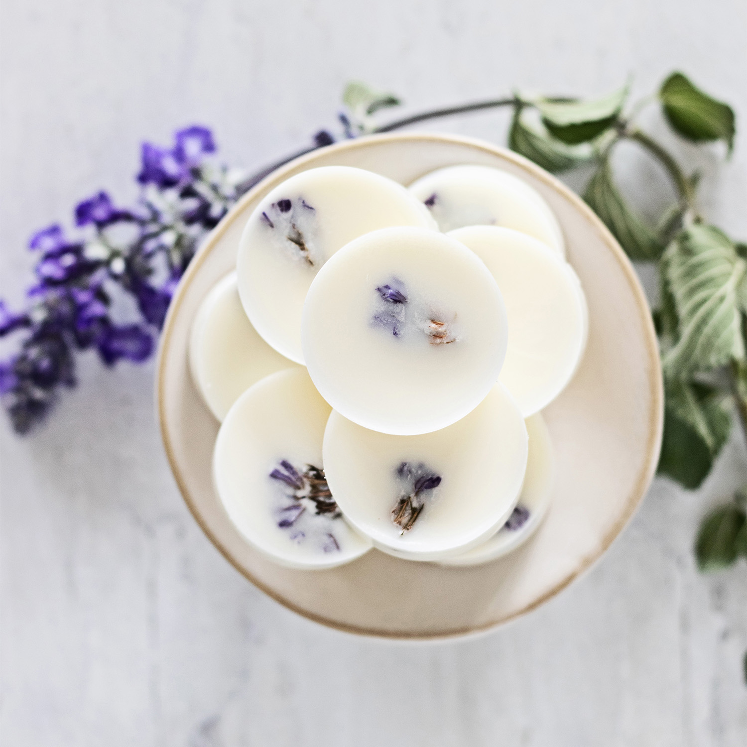 Looking down on a pedestal of creamy white, round wax melts with hidden purple-blue flowers showing through.