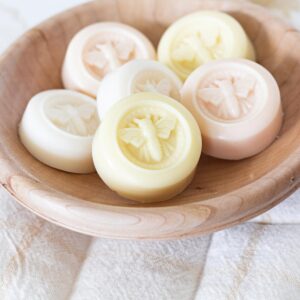 Handmade round soaps embossed with honey bees in a natural wood bowl.