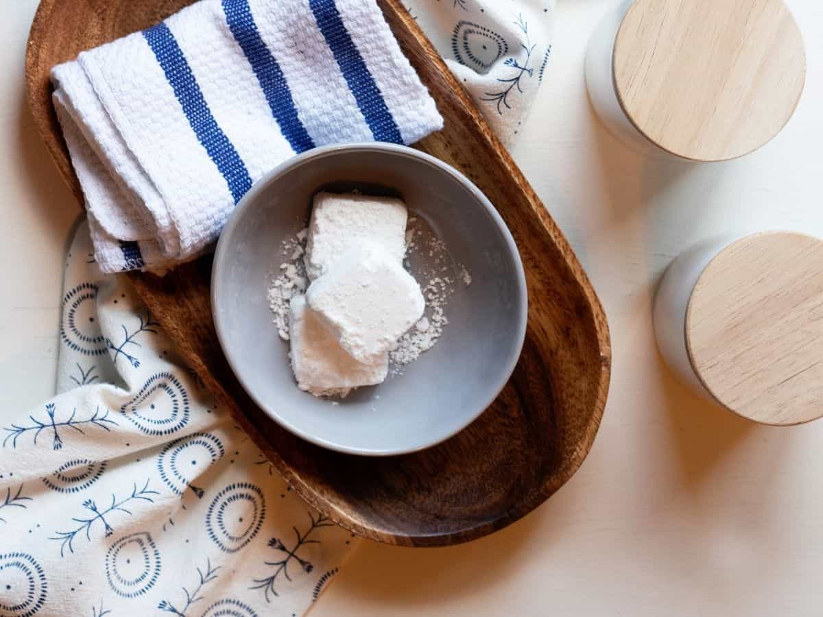 Small white garbage can deodorizer pods inside in a gray bowl on a wood tray