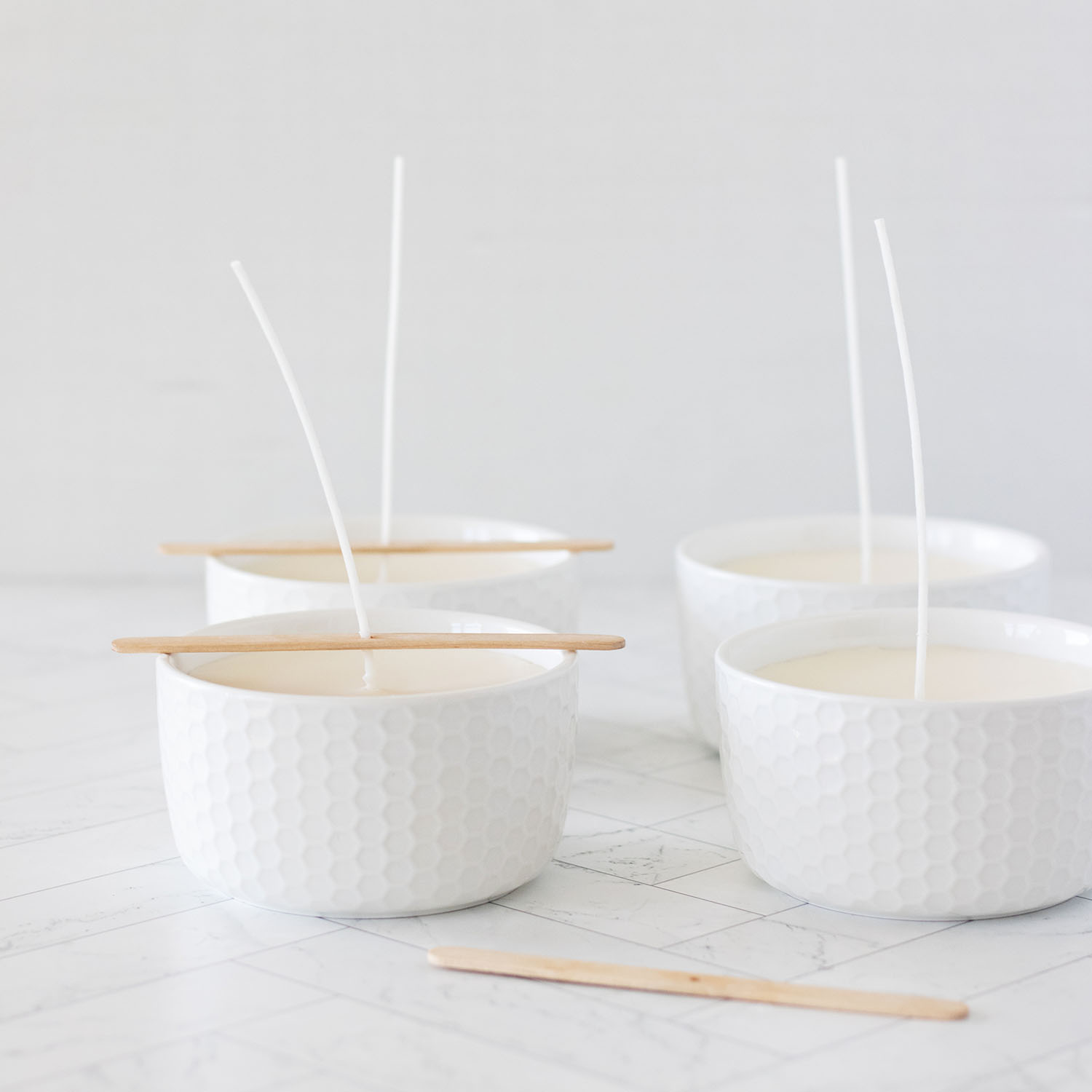 White candle bowls lined up curing with cotton wicks in centering sticks on white background
