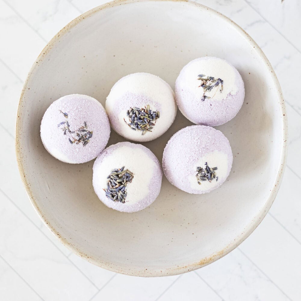 closeup on a bowl of large purple and white bath bombs with dried lavender