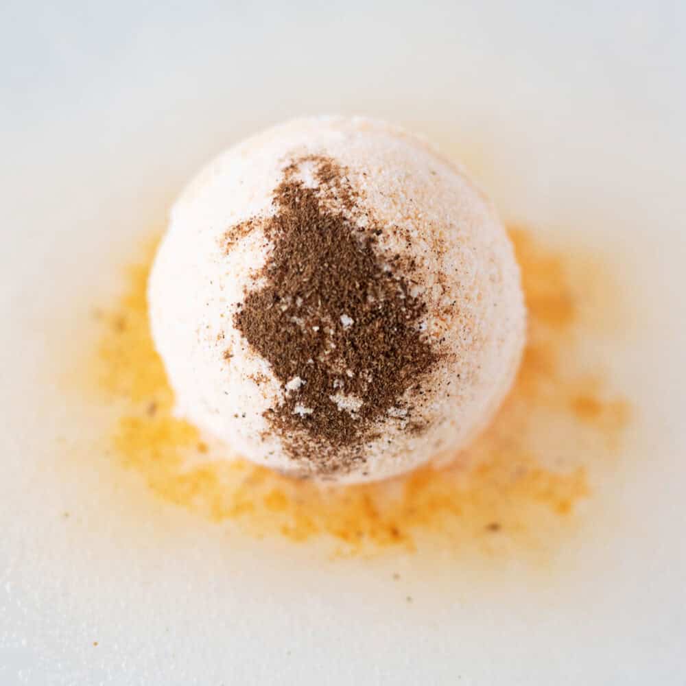 closeup of orange bath bomb fizzing in bath with ground spices on the top