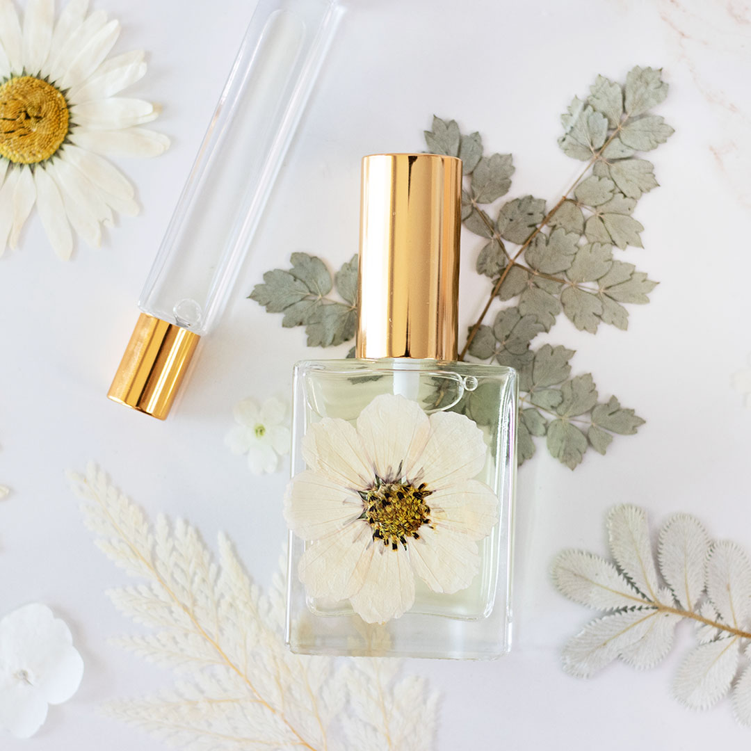 close up of glass perfume bottles with gold caps on top of pressed flowers