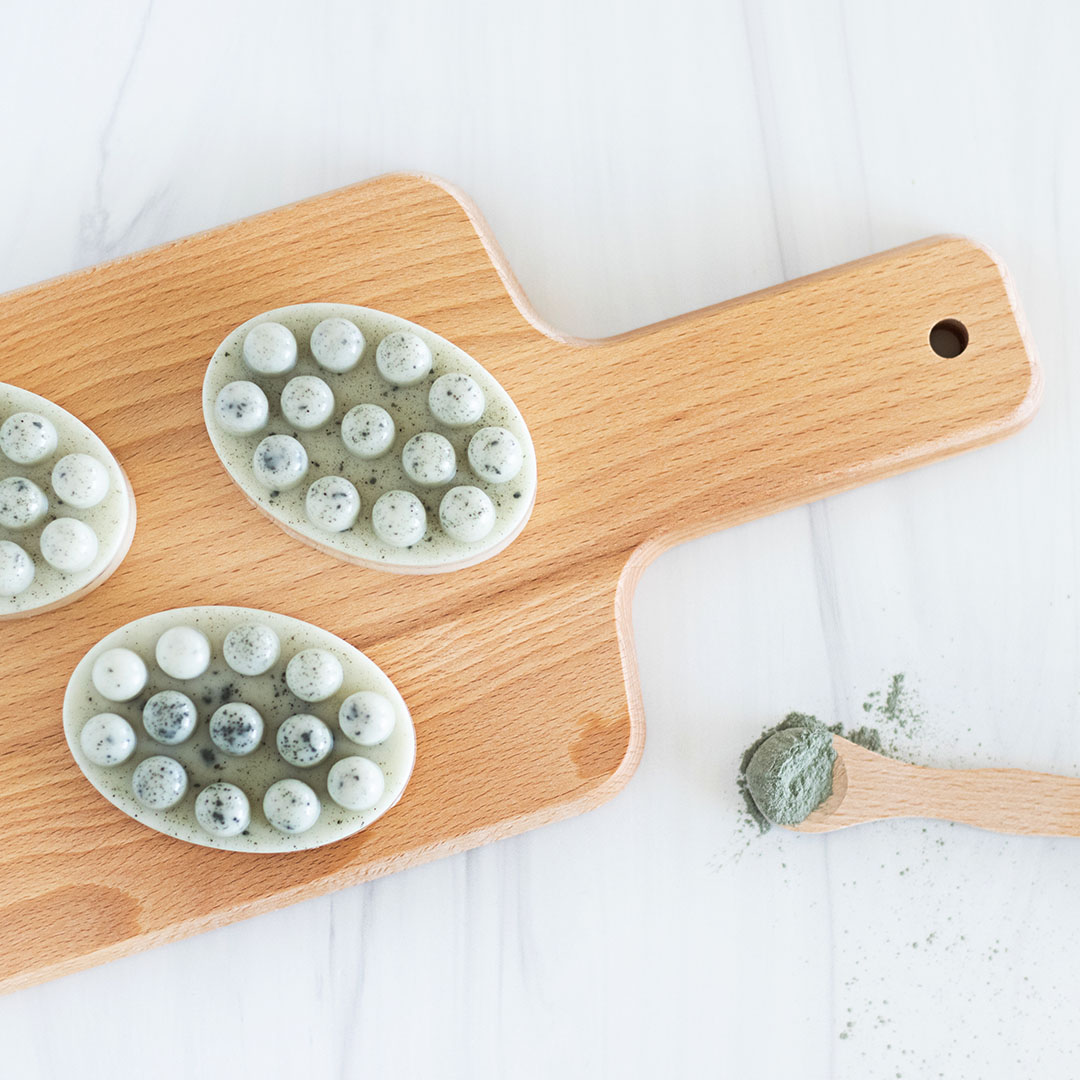 Robin eggs blue massage soap bars on a wood cutting board with a spoon scoop of Cambrian blue clay.