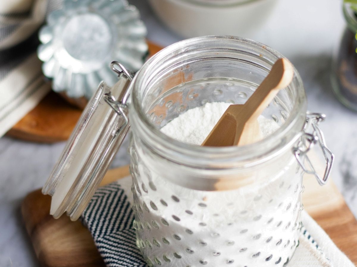 Looking into a jar of homemade dishwasher detergent with a wood scoop inside the jar
