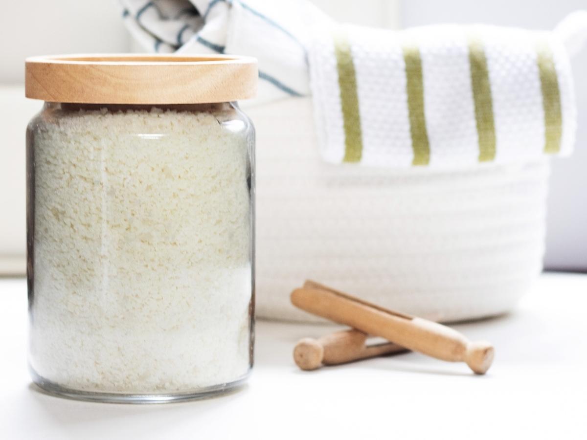 Large jar filled with homemade laundry detergent next to wooden clothespins.