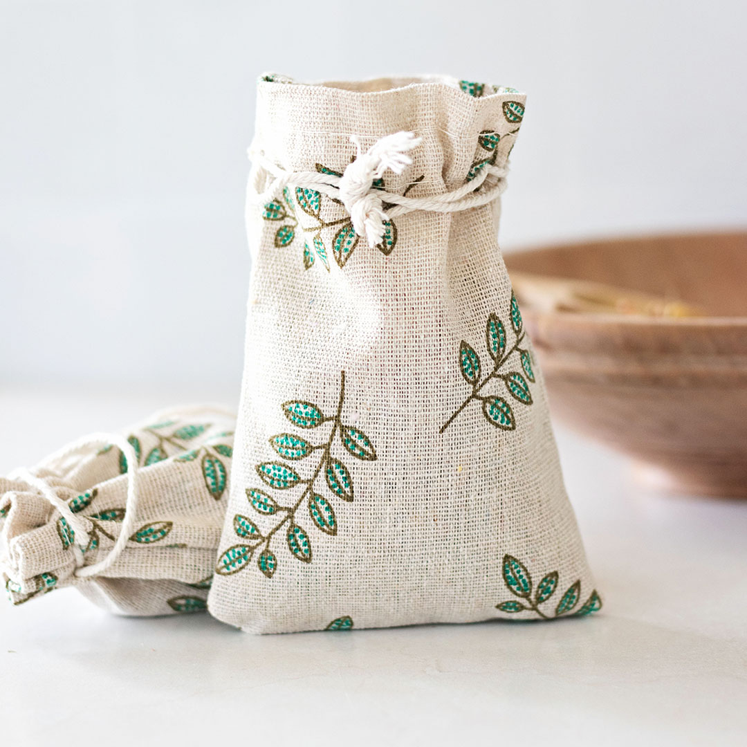 two cotton muslin drawstring sachets with a green leaf pattern next to a wooden bowl.