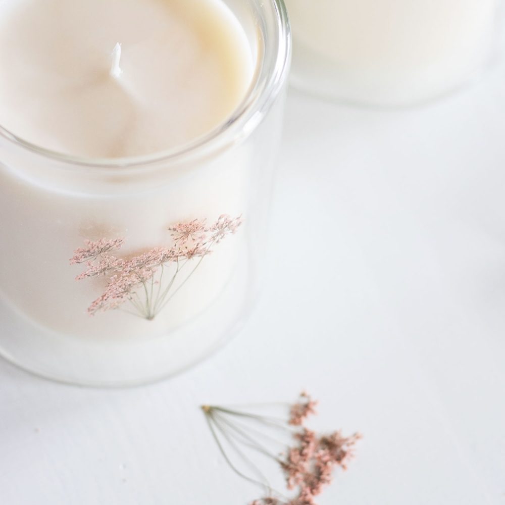 2 white candles in large glass jars with pink pressed flowers