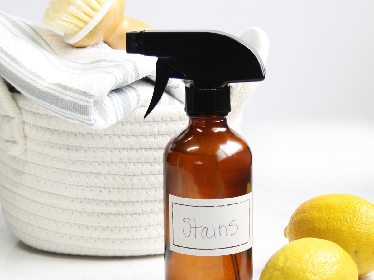An amber glass spray bottle of DIY natural stain remover next to a laundry basket