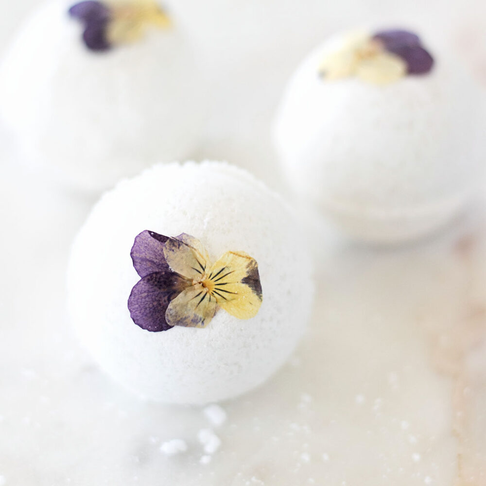three pressed violet pansy flowers on bath bombs on a marble counter