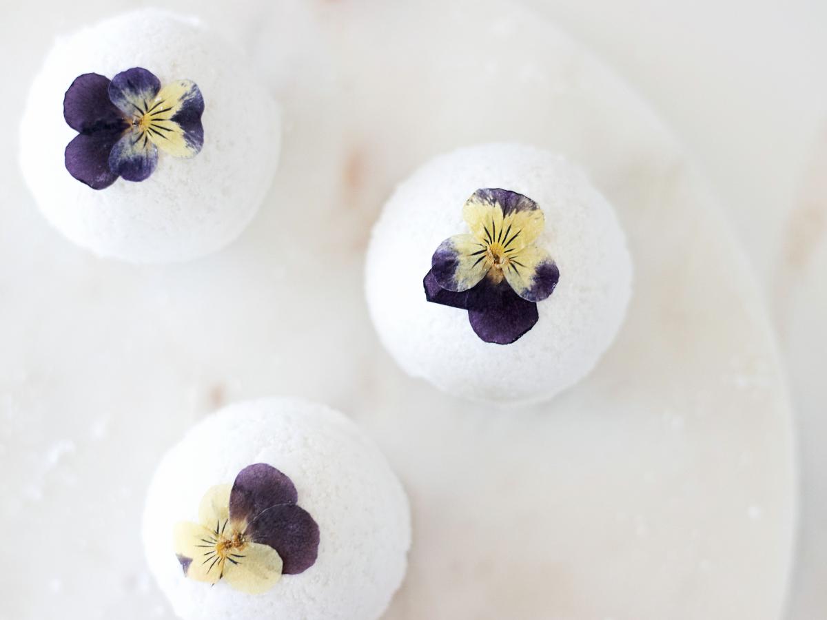 three pressed violet pansy flowers on bath bombs on a marble counter
