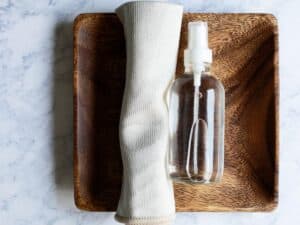 small clear glass bottle of DIY stainless steel spray on a wooden tray next to a small microfiber cloth
