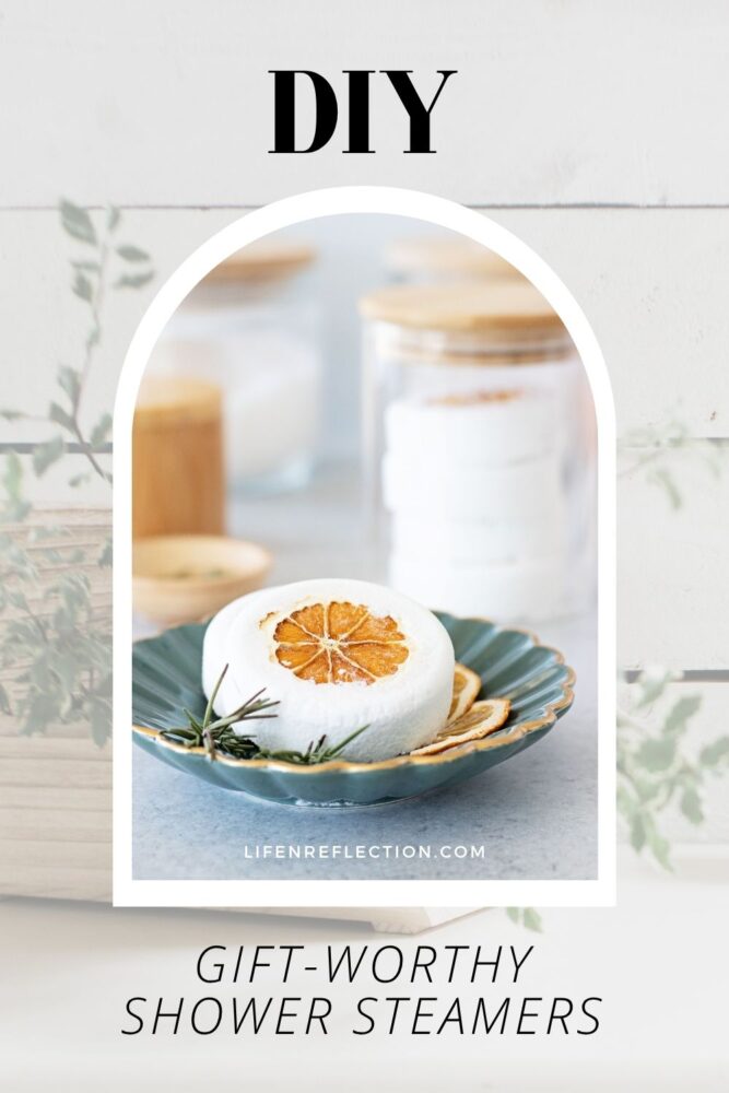 Close up of a large round diy shower steamers embedded with a dried orange slice and rosemary sprigs in a ceramic tray.