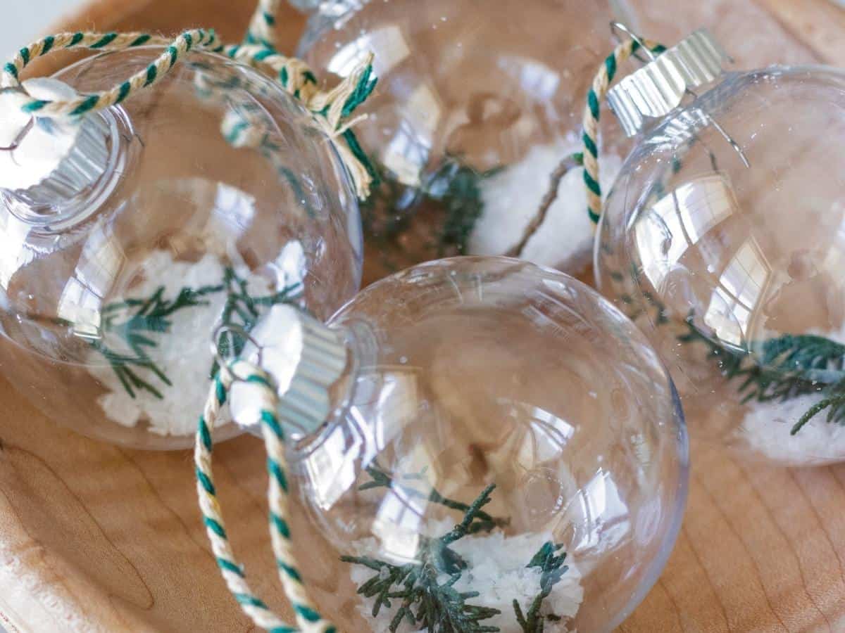 closeup of diy glass ornaments filled with juniper clippings and snowy salt flakes in a wooden bowl