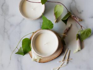 scented candles in white ceramic bowls surrounds by honeysuckle flower stems and match sticks on a marble counter top