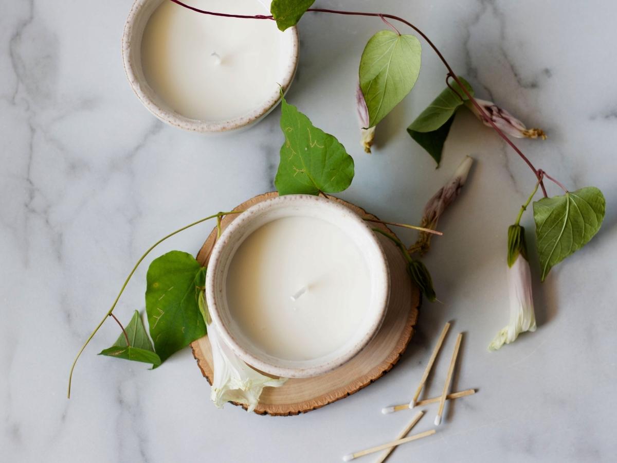 scented candles in white ceramic bowls surrounds by honeysuckle flower stems and match sticks on a marble counter top