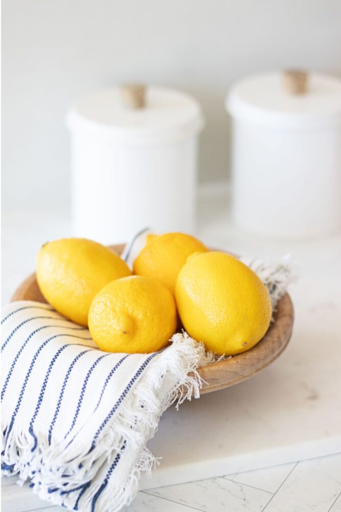 wooden bowl of fresh lemons on a kitchen countertop in soft sunlight in front of storage jars.
