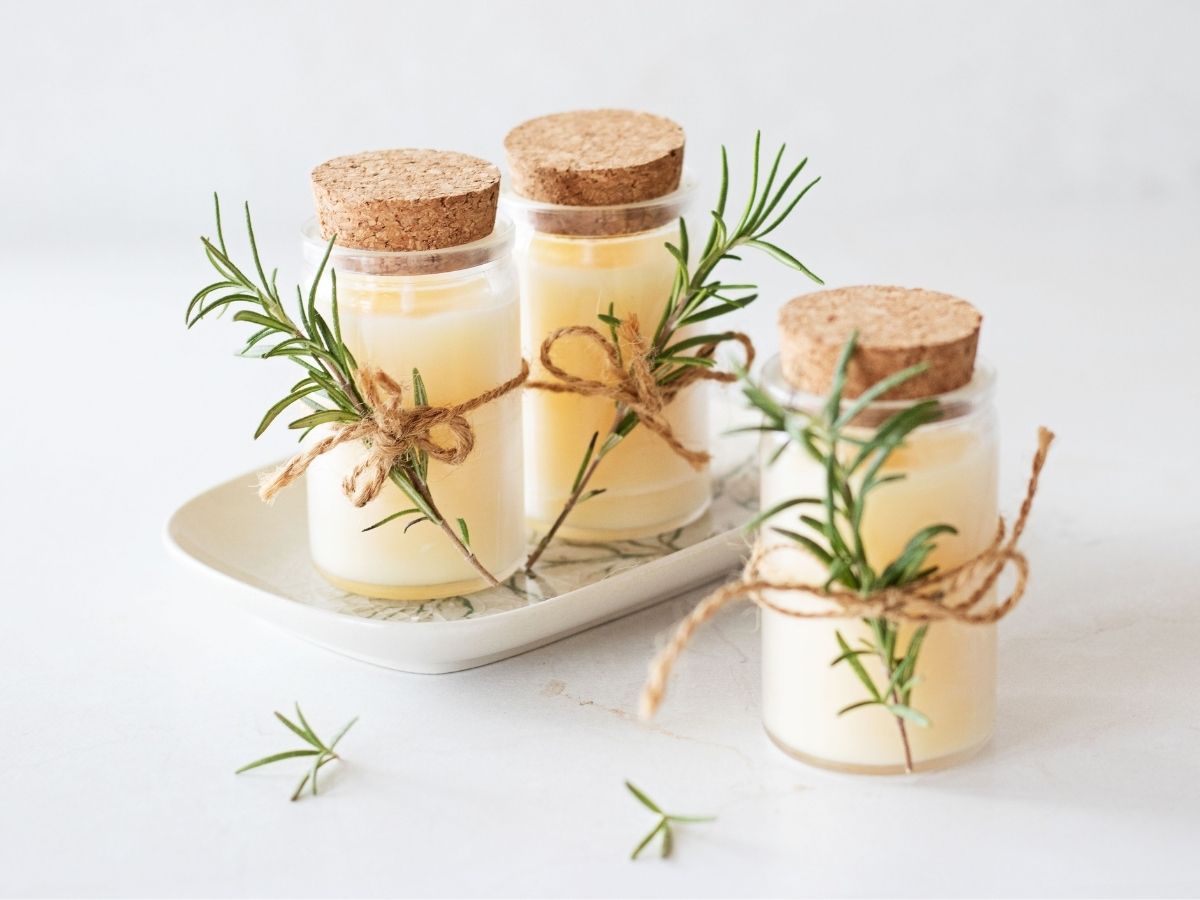 trio of beeswax candles in glass spice jars wrapped with fresh rosemary and twine on a white background