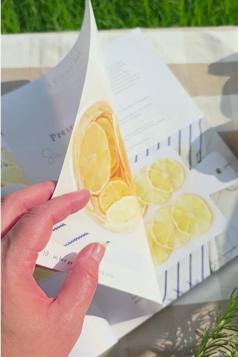 Turning the pages of In Her Garden Magazine on gingham picnic blanket.